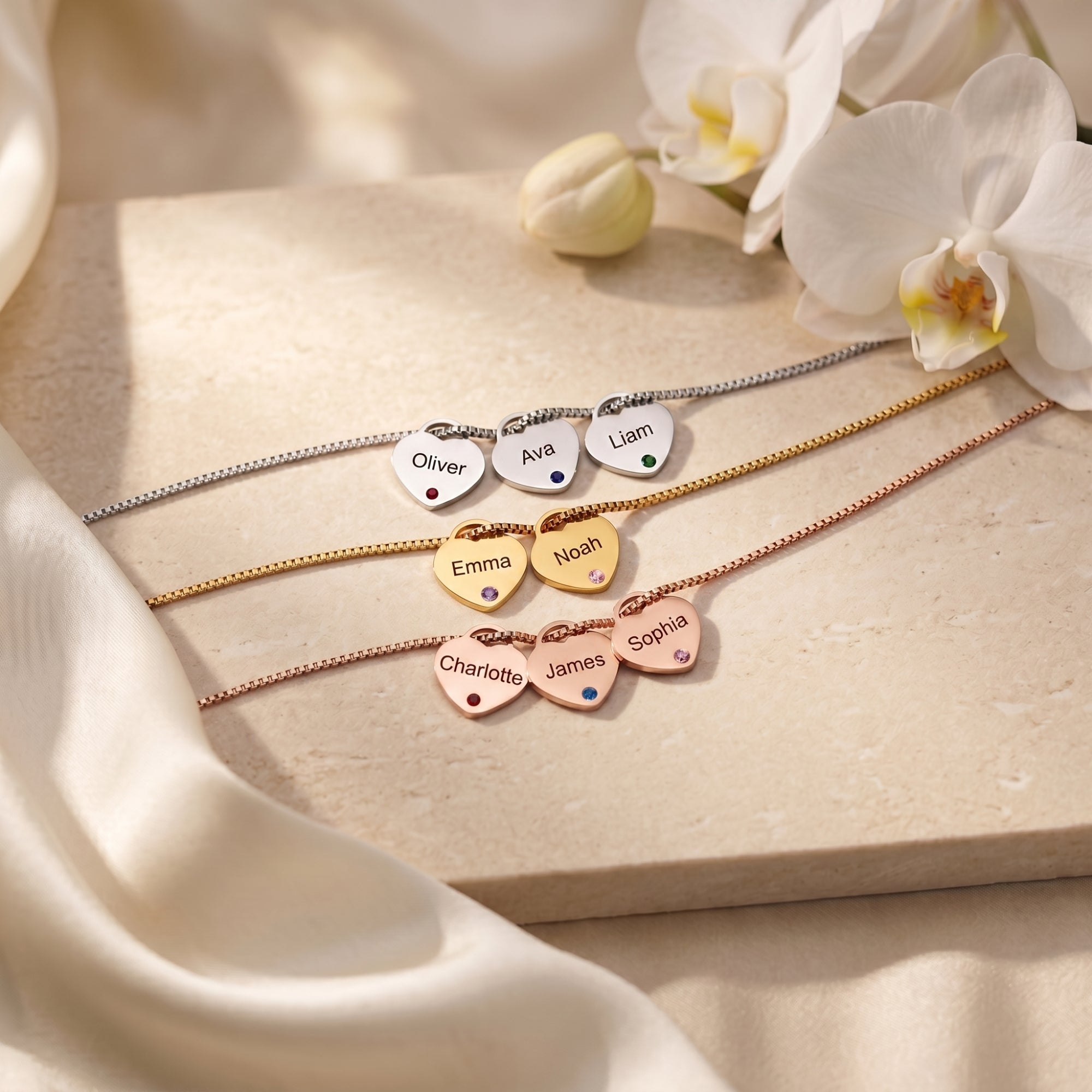 Three Sybilla necklaces in silver, gold, and rose gold with engraved heart pendants and birthstones on stone.
