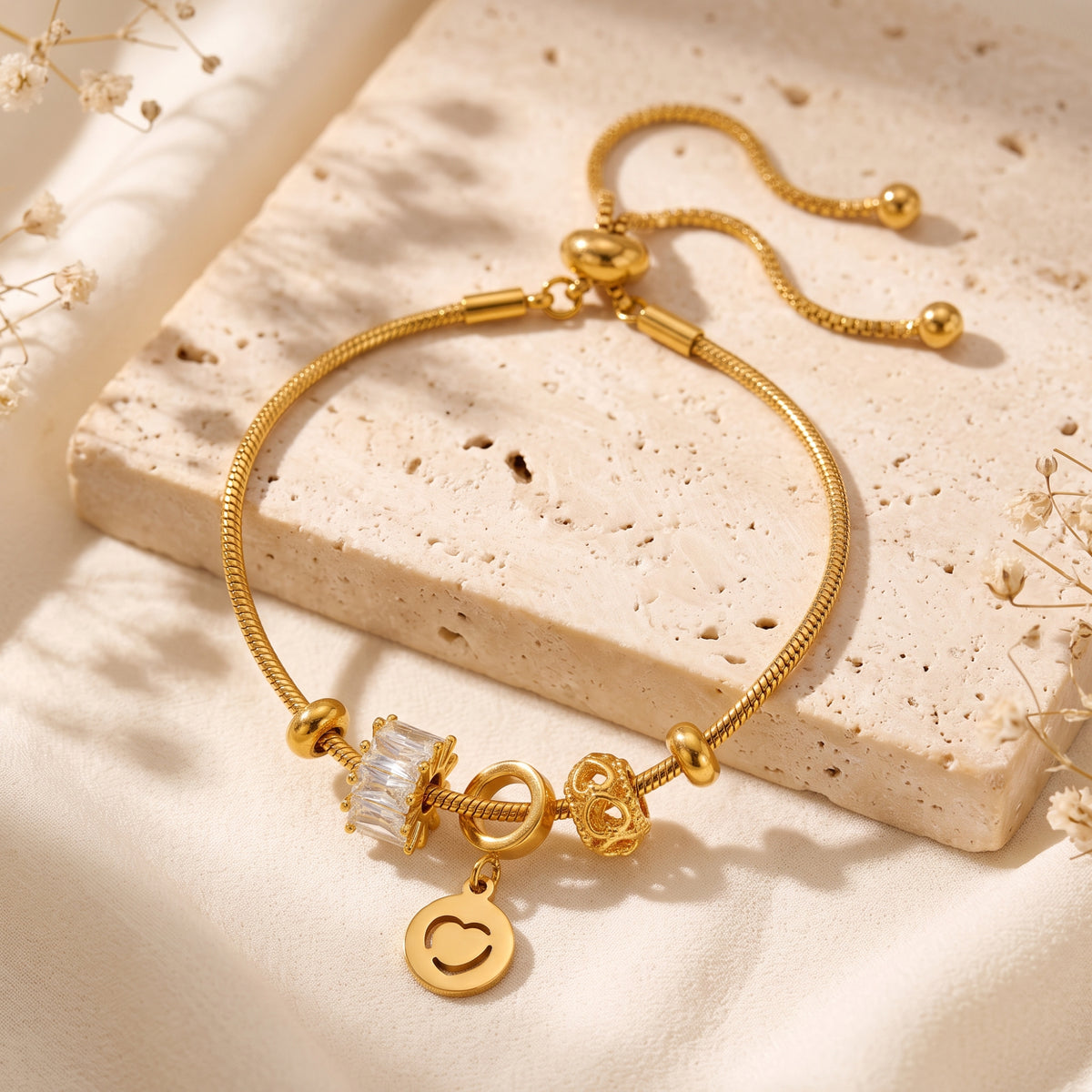 Gold-tone heart charm bracelet with bolo slider clasp set flat on a textured stone block.
