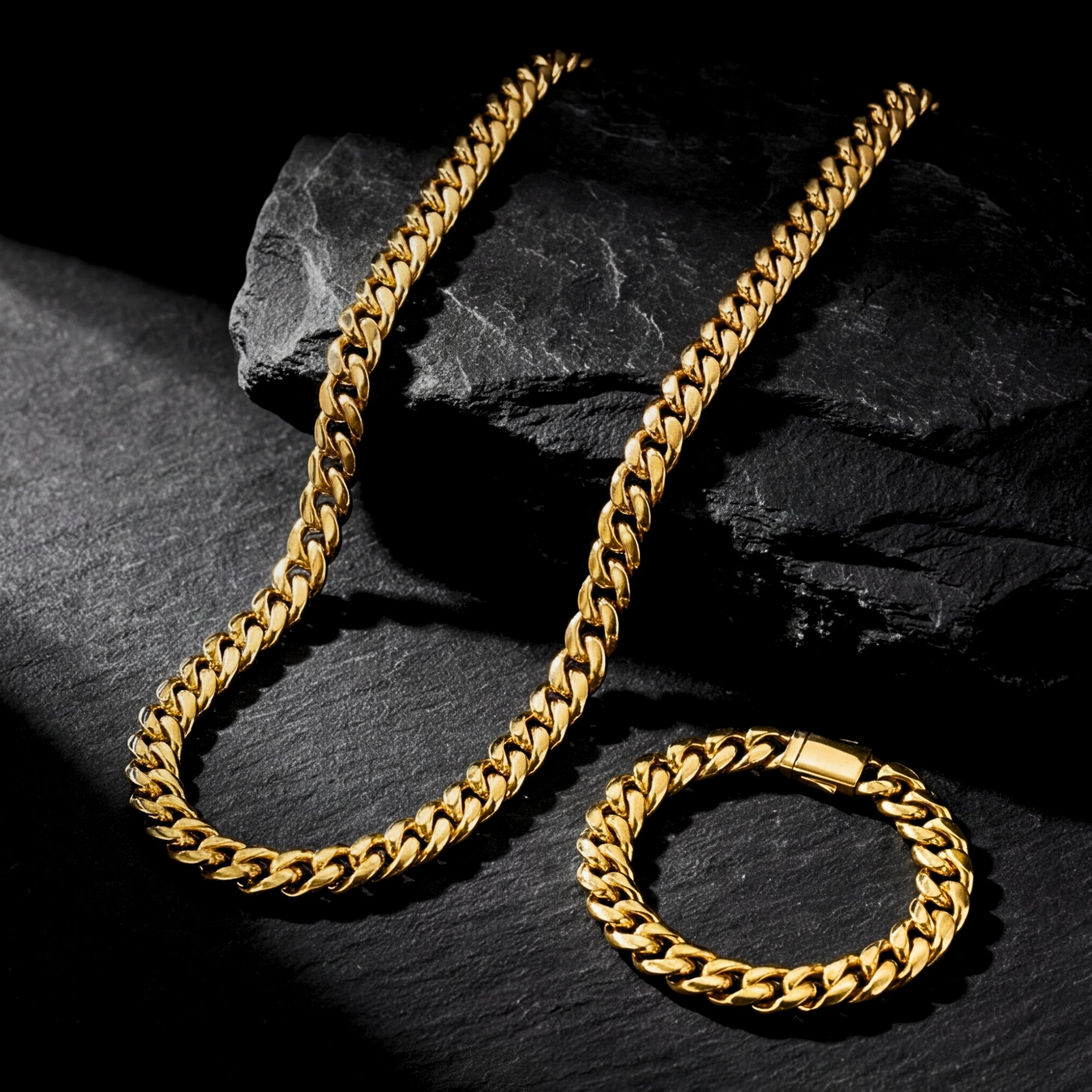 Gold stainless steel 8mm Cuban link chain and bracelet set styled on dark, textured rocks.
