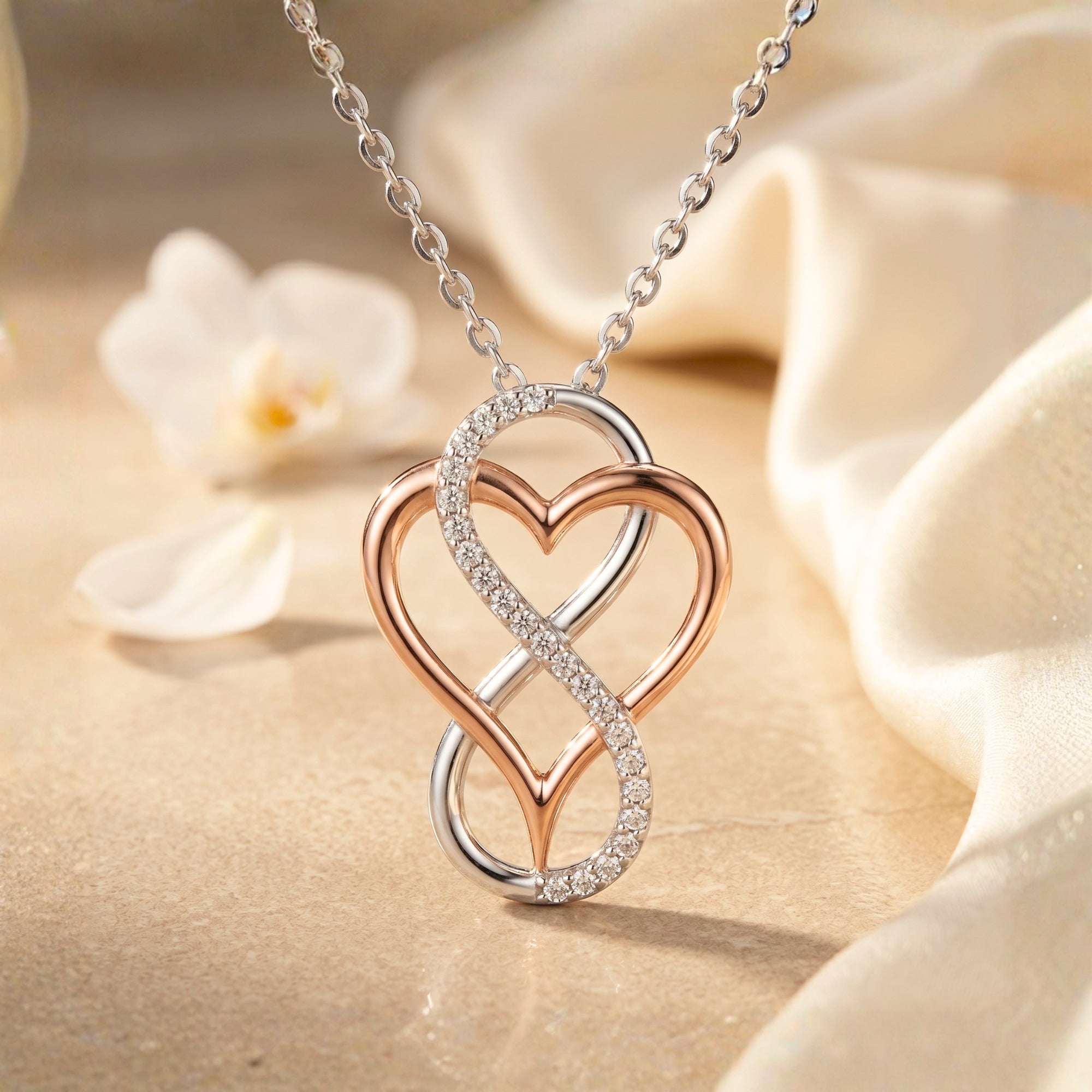 Infinity heart moissanite pendant necklace in solid gold on a draped fabric background.