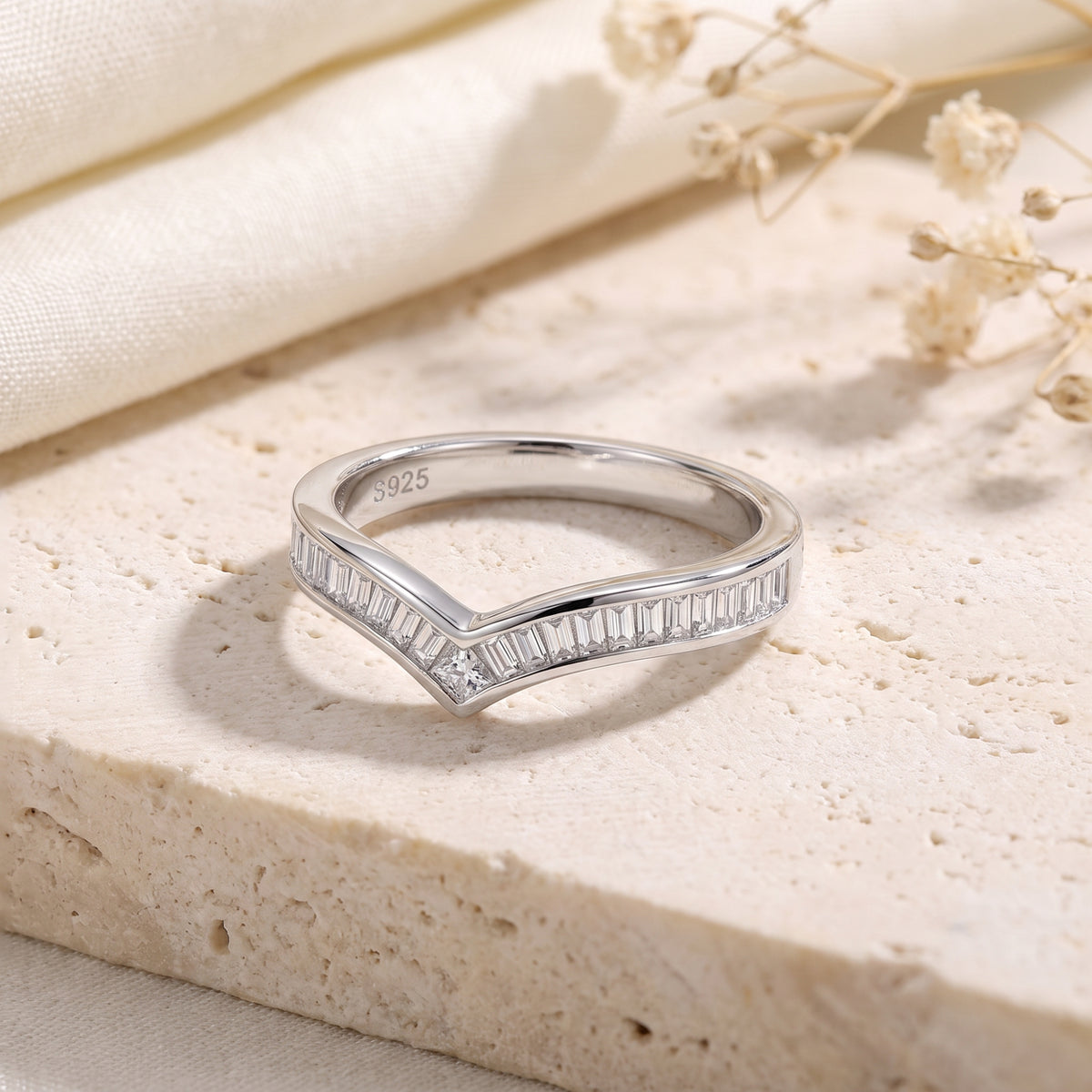 Close-up of a silver chevron ring with channel-set baguette stones resting on a porous stone surface.
