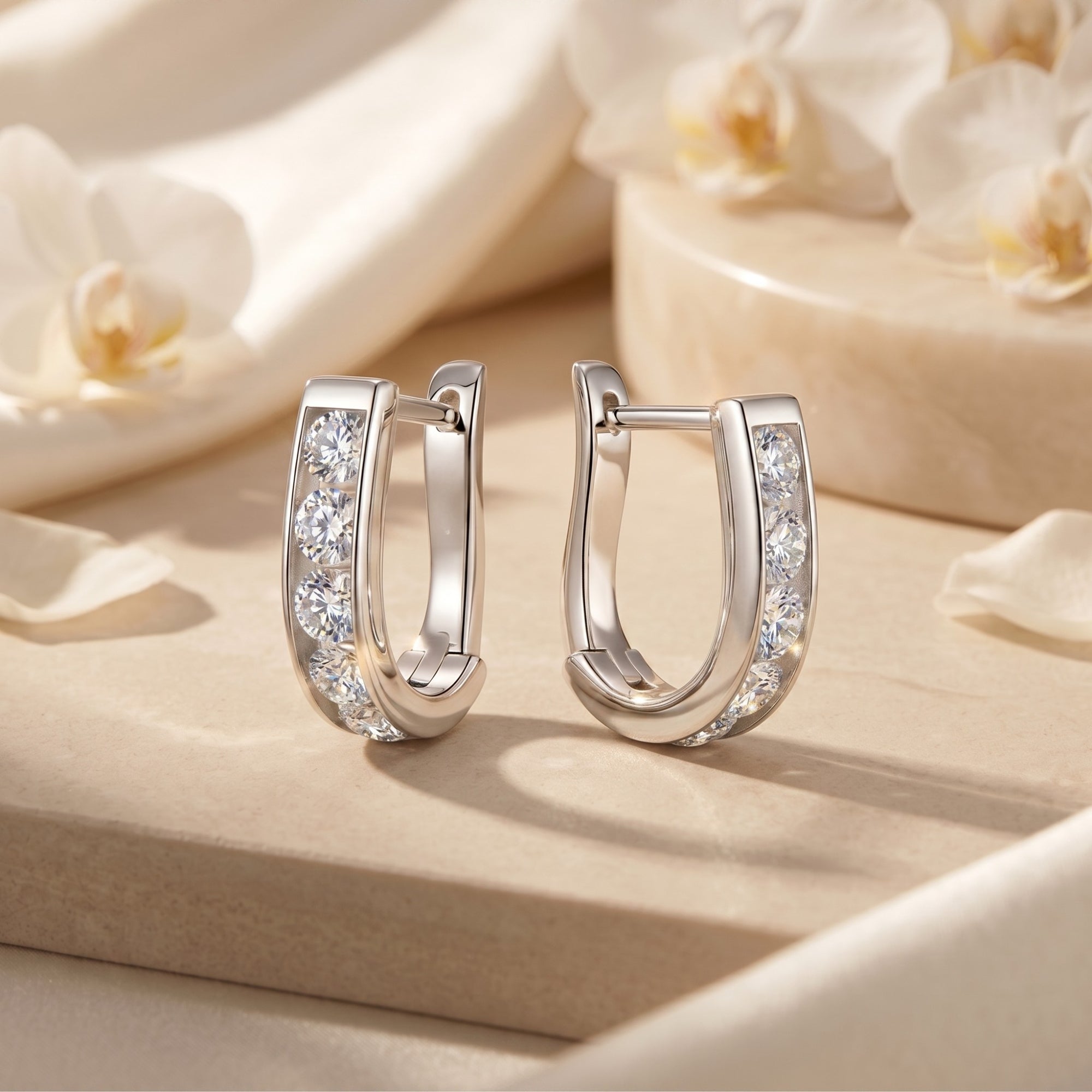 Silver moissanite hoop earrings with round stones on a stone surface with white flowers.