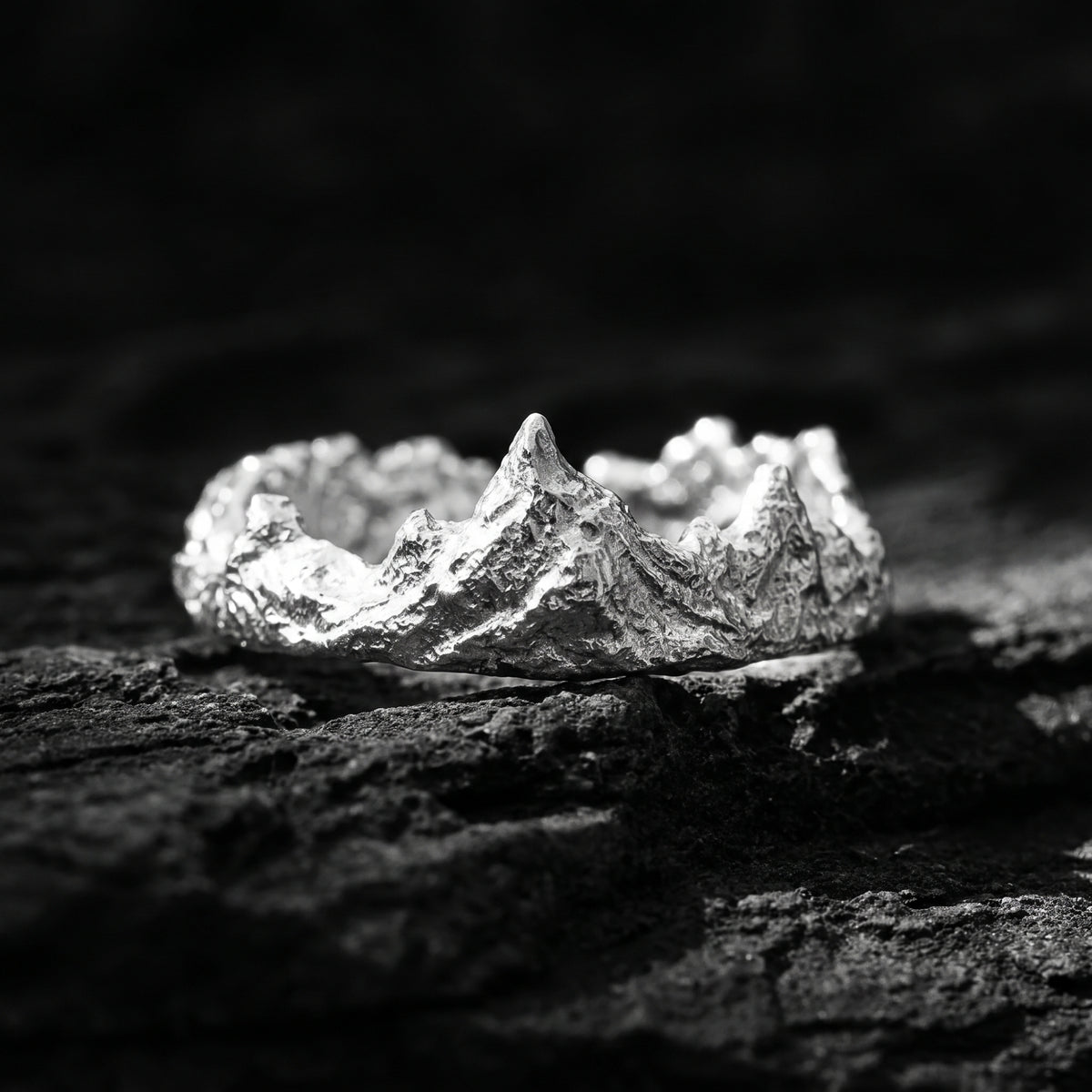 Sculpted 999 fine silver mountain crest ring resting on dark textured rock.