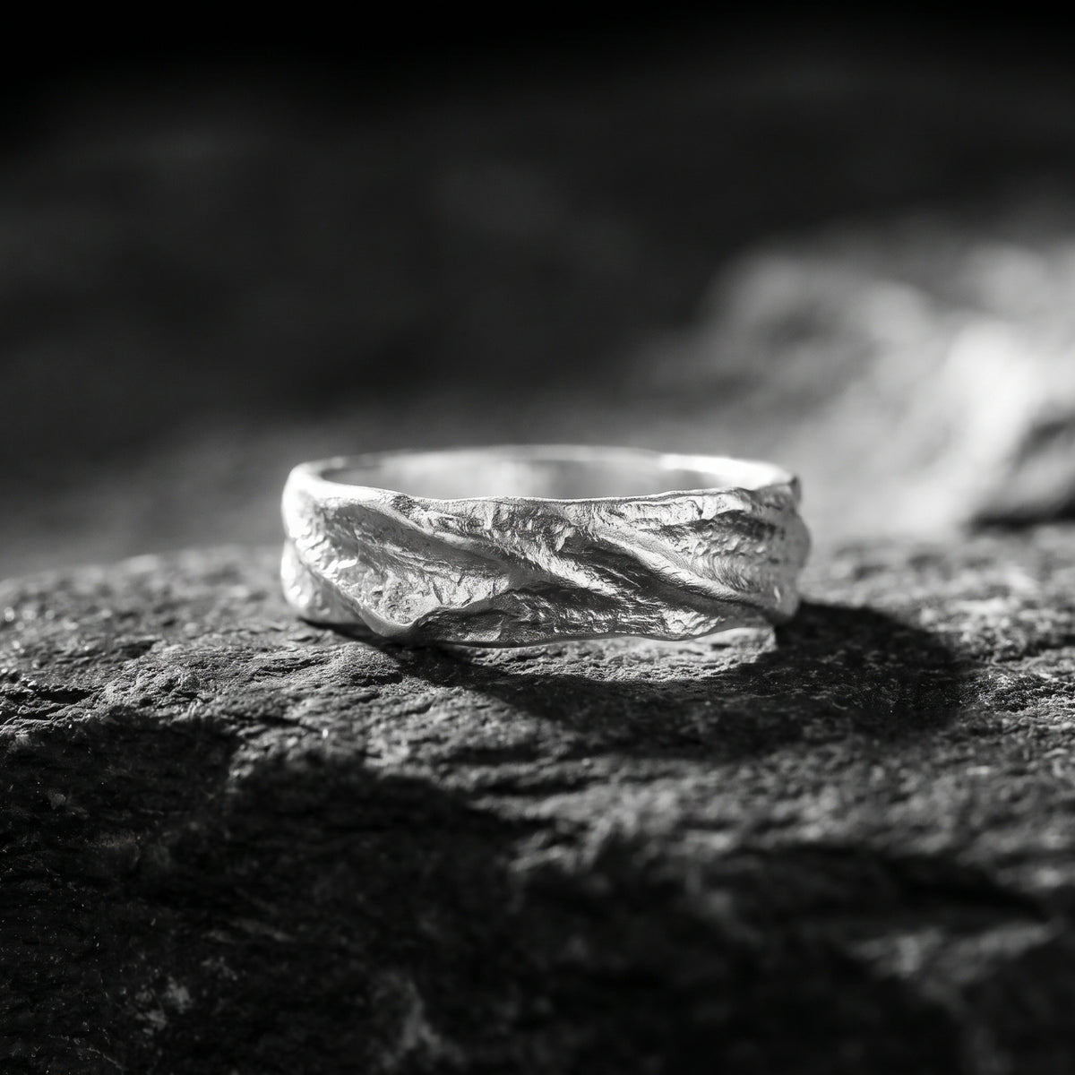 Close-up of a textured fine silver open band ring resting on rough dark rock.