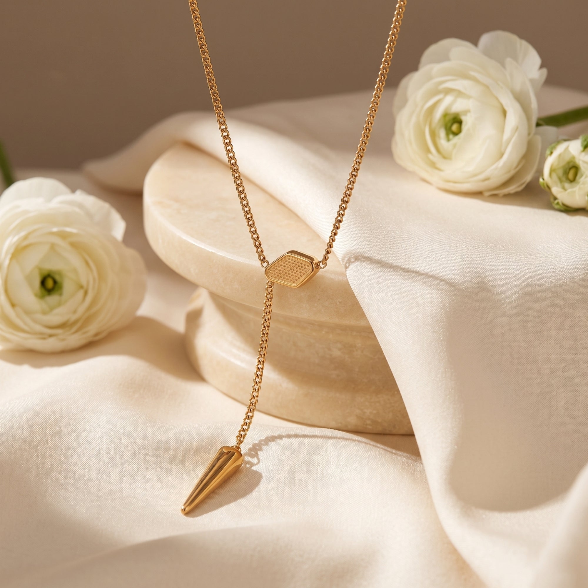 Gold stainless steel lariat necklace with hexagonal slider and spike pendant on styled fabric.