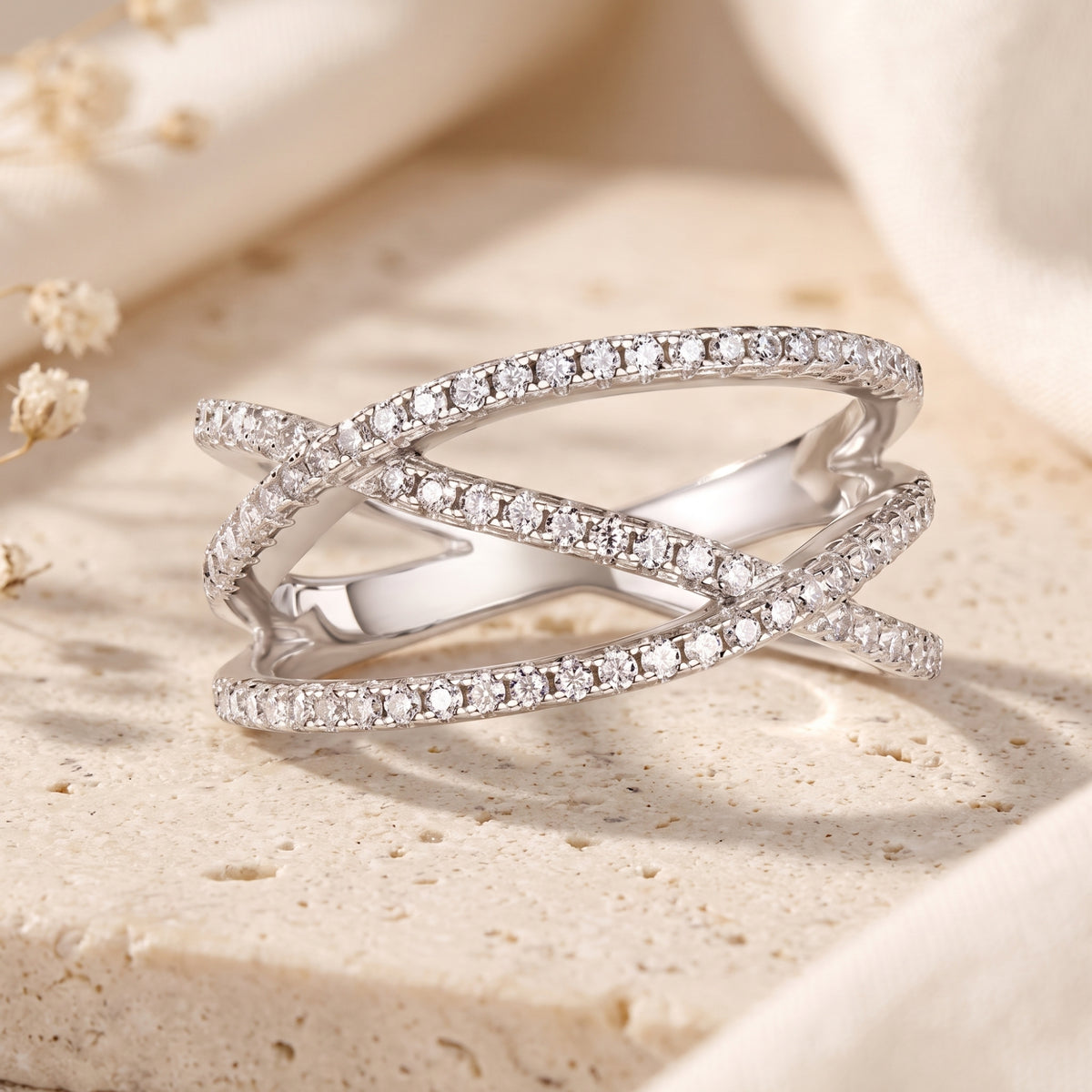 Silver crossover ring with interwoven bands lined with clear pave stones on a textured surface.