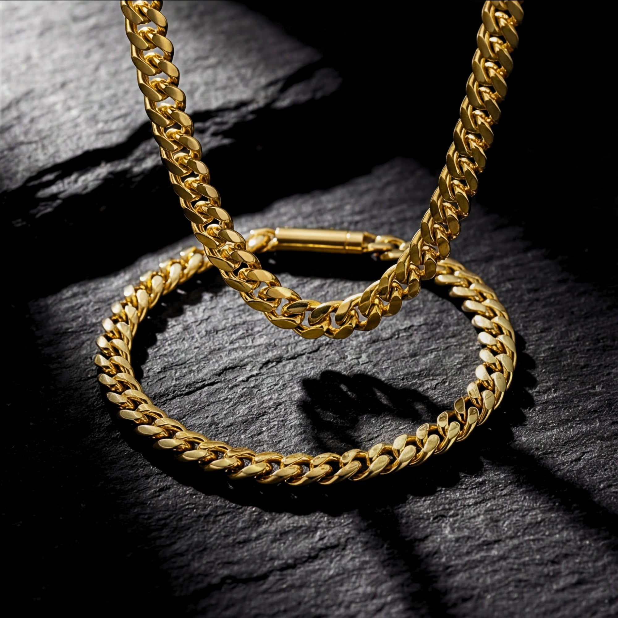 Gold stainless steel 6mm Cuban link chain and bracelet set displayed on a dark textured stone surface.