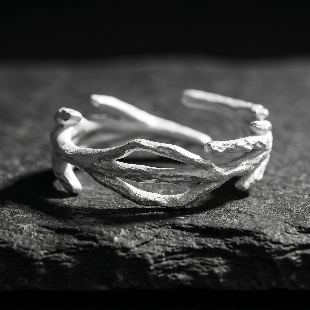 Front macro view of the silver open branch ring resting on dark textured rock, showing its intertwined rough-textured bands.
