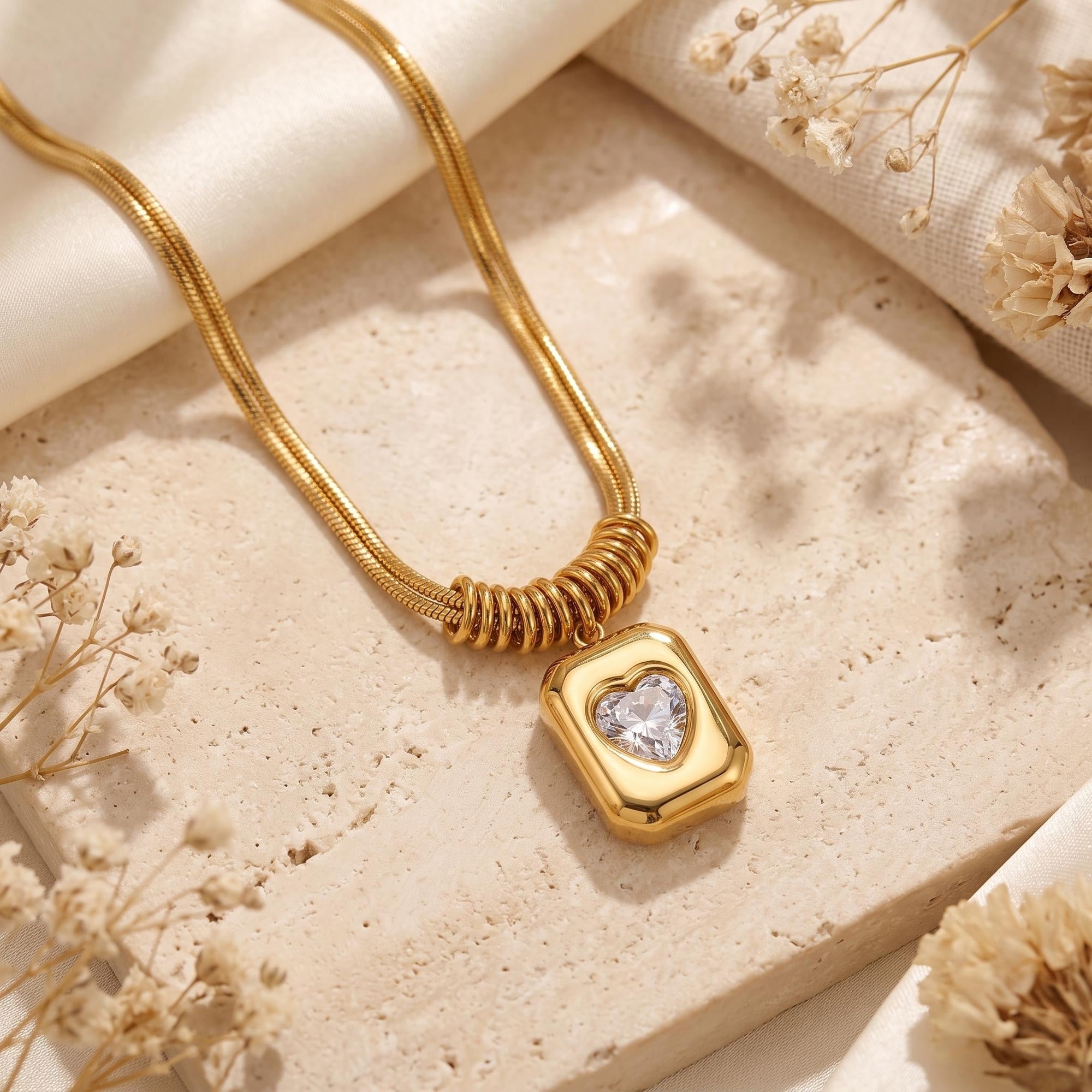 Gold Sophia Heart Necklace with a heart-cut simulated diamond on a textured stone surface with dried flowers.