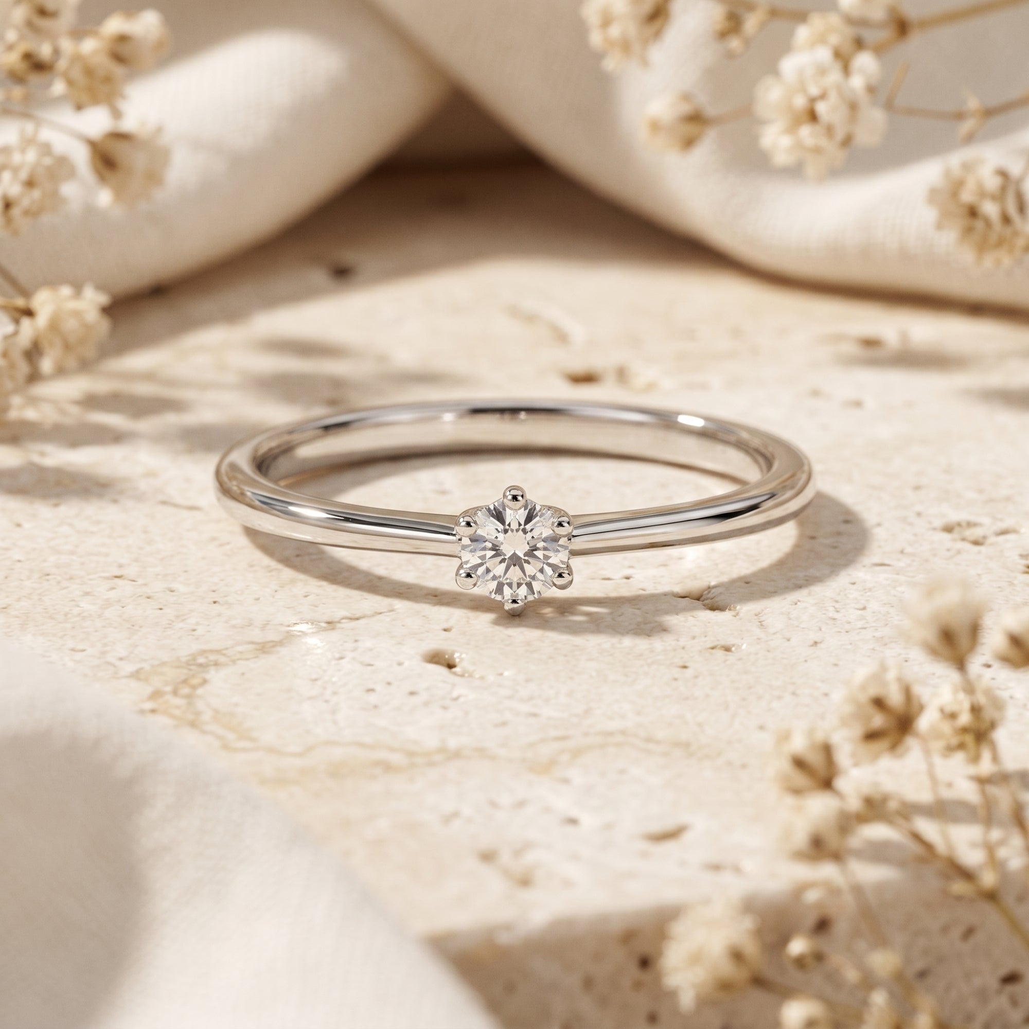 Round cut moissanite solitaire ring in silver on stone with flowers.