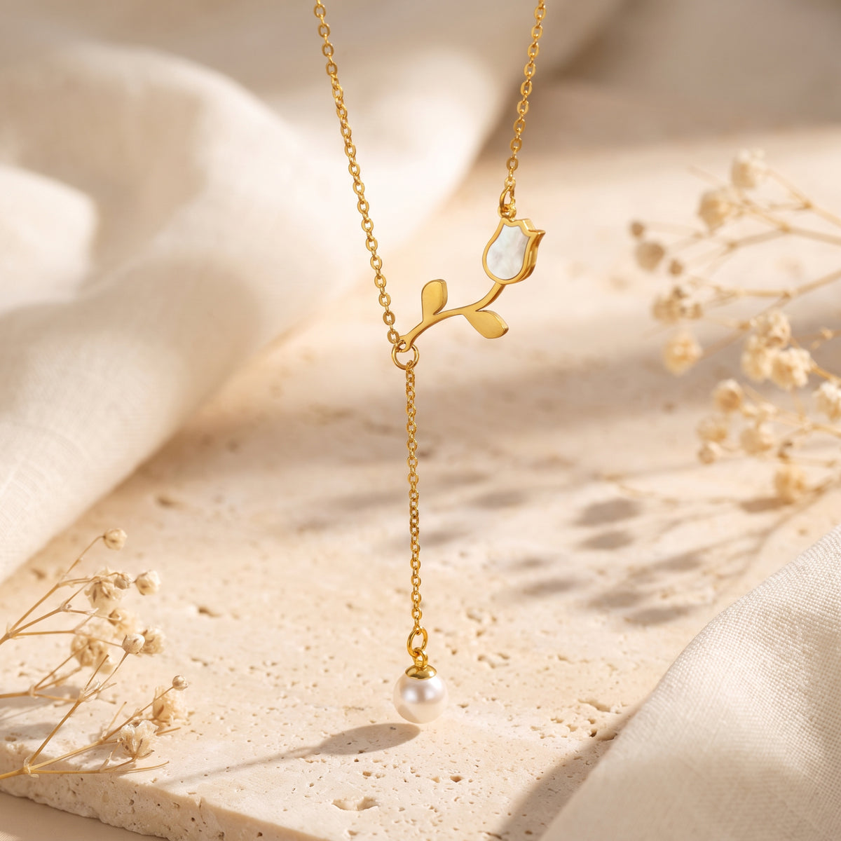 Vertical macro view of a gold-tone tulip lariat necklace with mother-of-pearl inlay and dangling pearl.