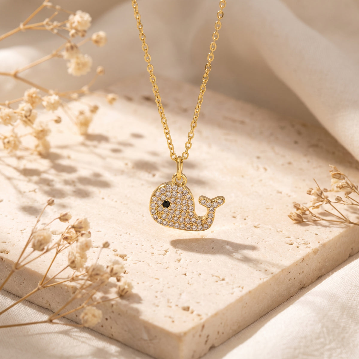Gold-tone whale pendant set with pave crystals, hanging suspended over a stone surface.