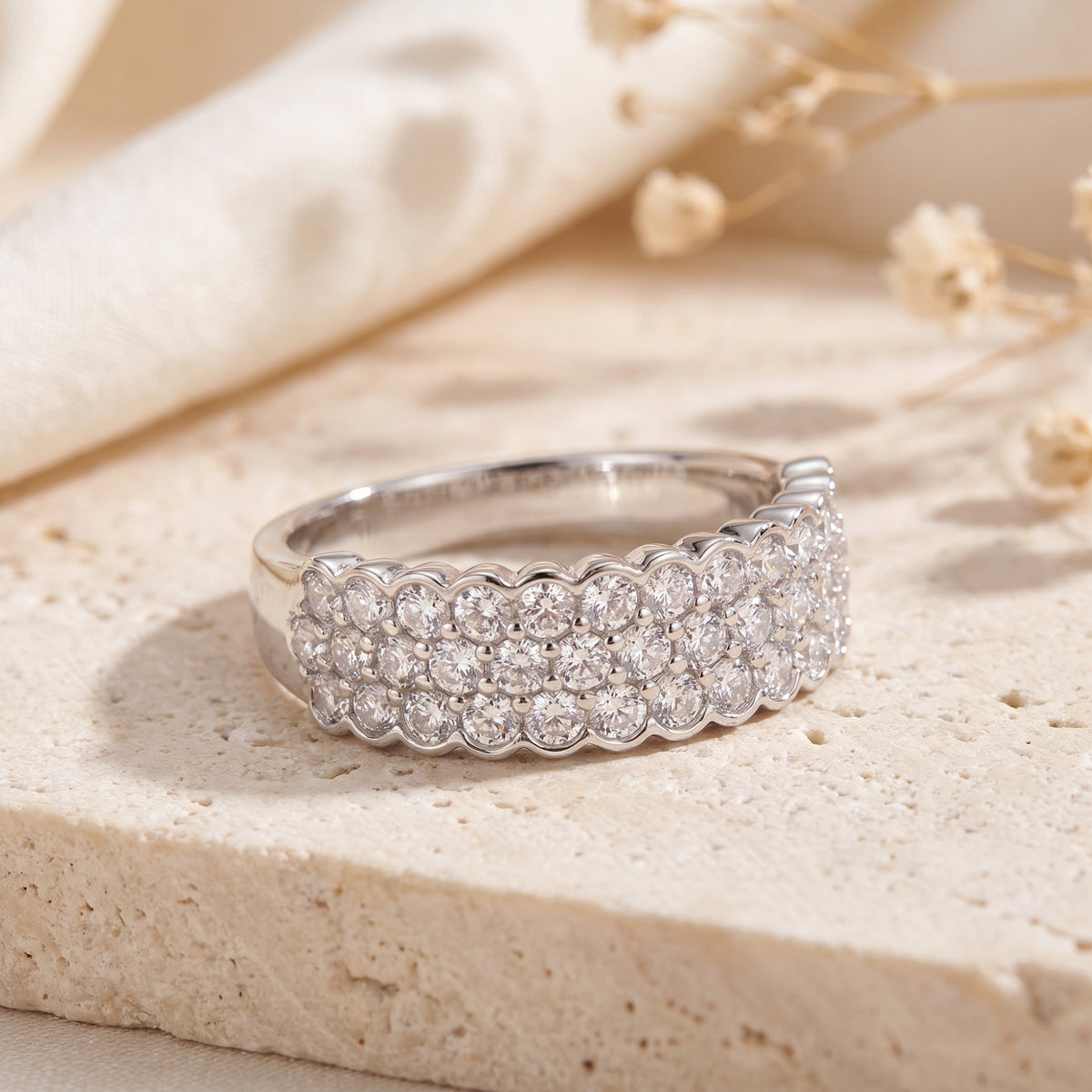 Angled close view of a silver scalloped triple-row clear-stone ring resting on a beige stone slab.