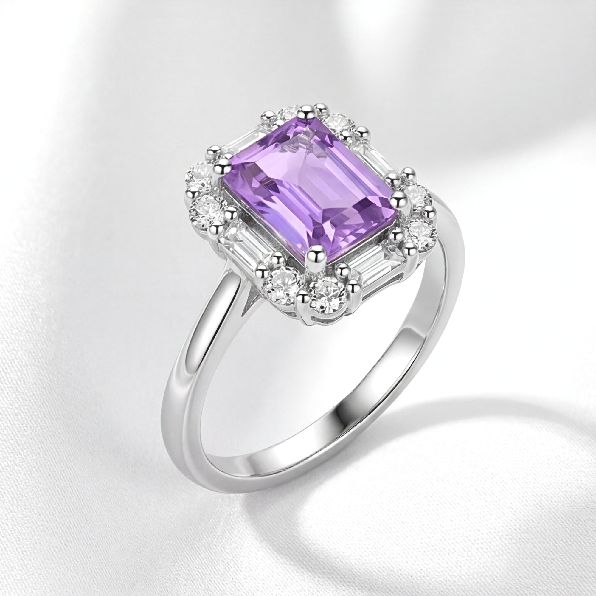 Emerald cut simulated amethyst halo ring in S925 sterling silver, angled view on white silk fabric.