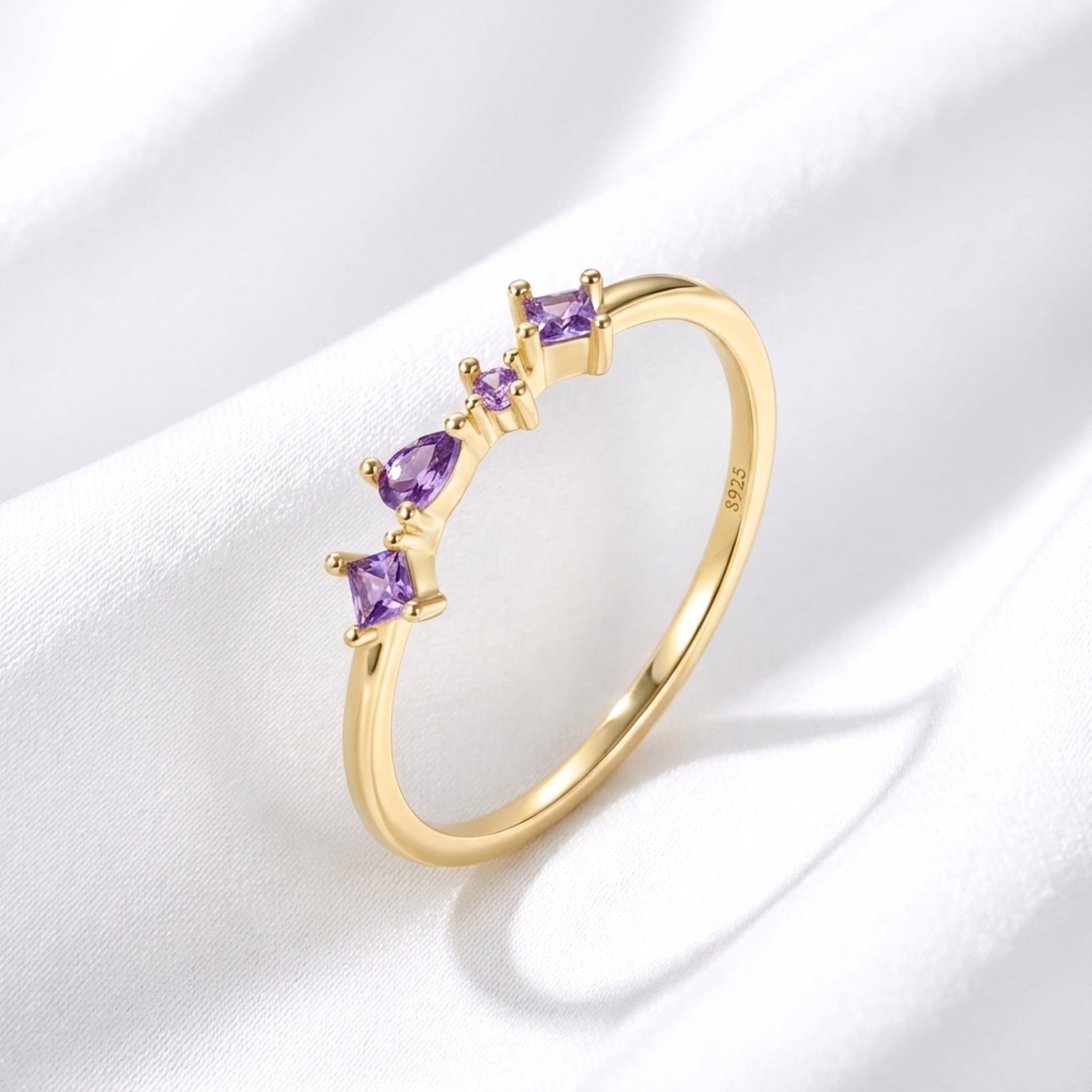 Elisia 18K gold vermeil ring with princess and pear cut simulated amethyst on white draped fabric.