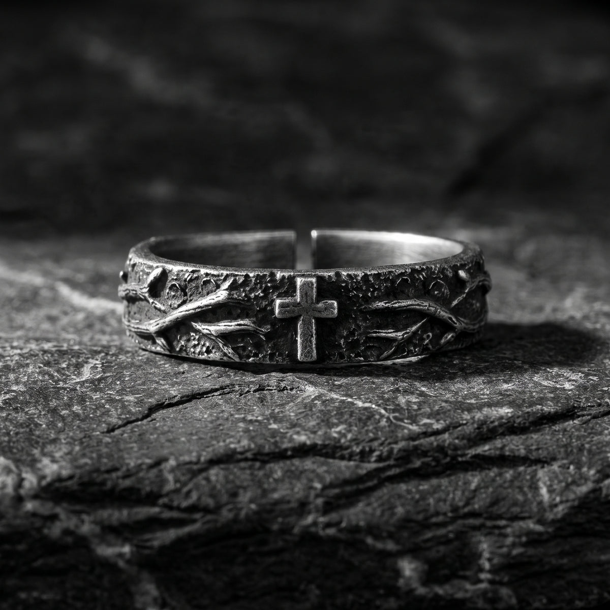 Front view of a silver open-band ring with thorn texture and a central cross, resting on dark slate