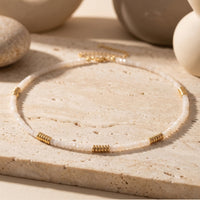 White quartz beaded necklace with gold-tone grooved accents on a textured stone surface.