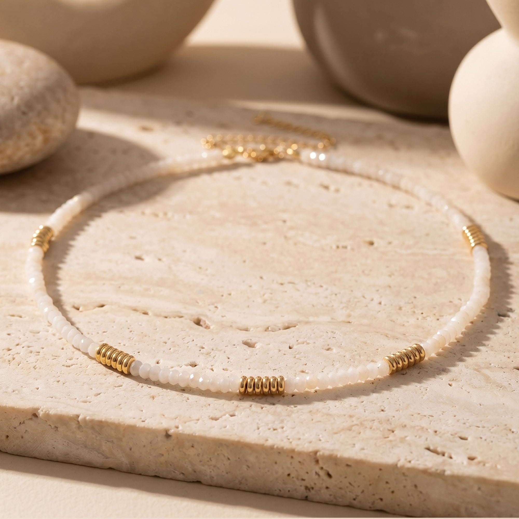 White quartz beaded necklace with gold-tone grooved accents on a textured stone surface.
