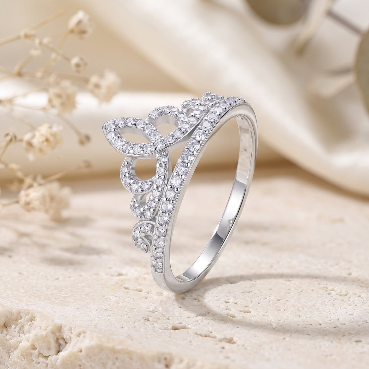 Silver tiara crown ring with cubic zirconia pave accents displayed upright on a textured stone surface.