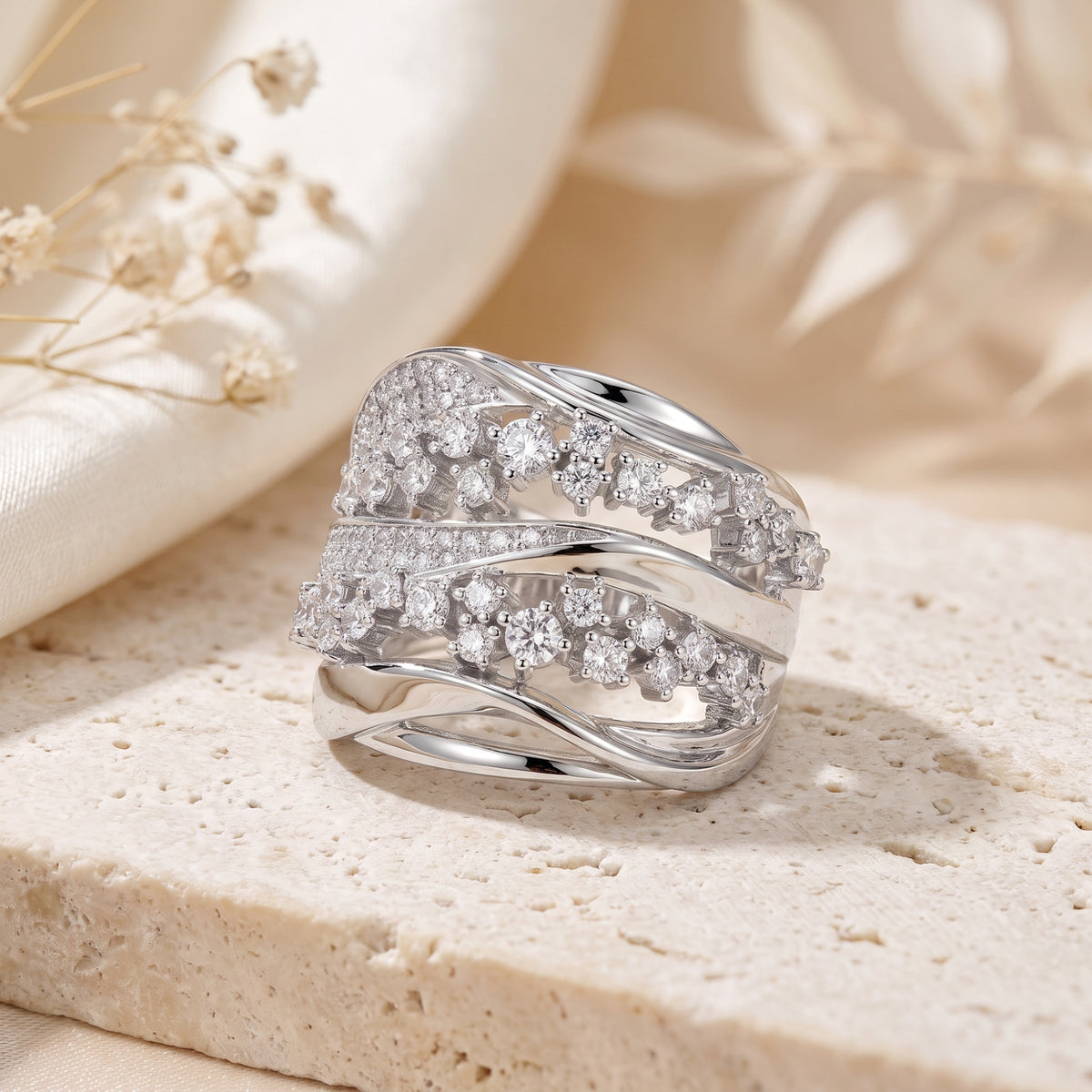 The Aurora Crossover Ring in silver with multi-row stone bands, set upright on a stone surface.