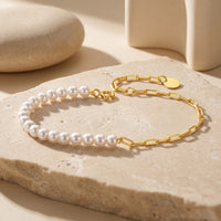 Solid gold O-chain and white cultured pearl bracelet displayed on a textured stone surface.