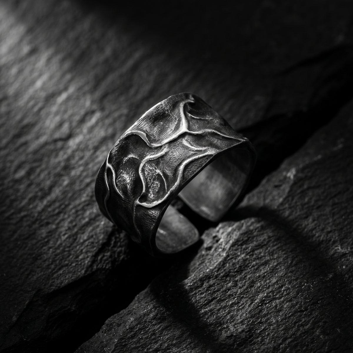 Close-up of the textured silver open band ring on slate rock, highlighting its molten surface.