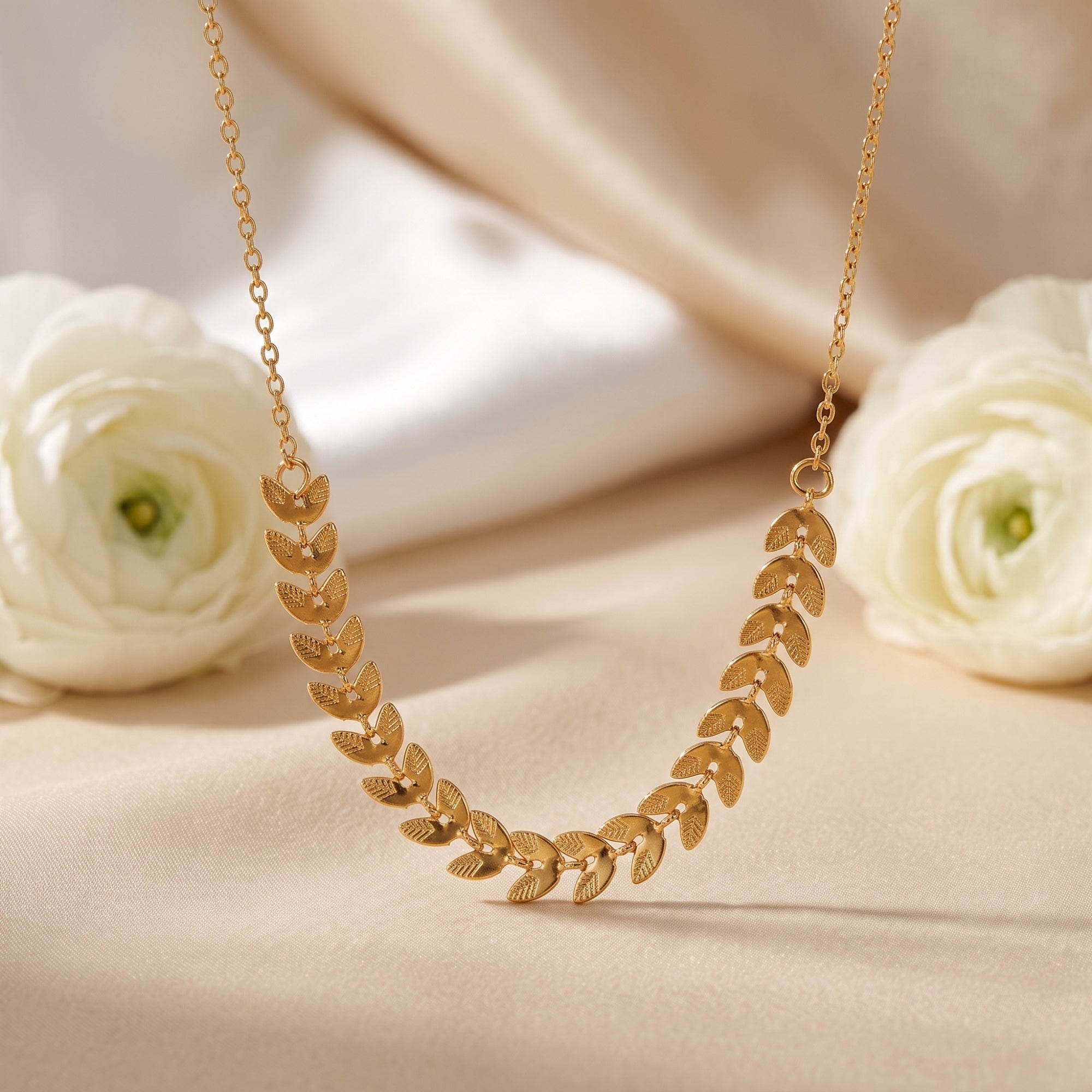 Gold leaf bib necklace on cream silk with white flowers.