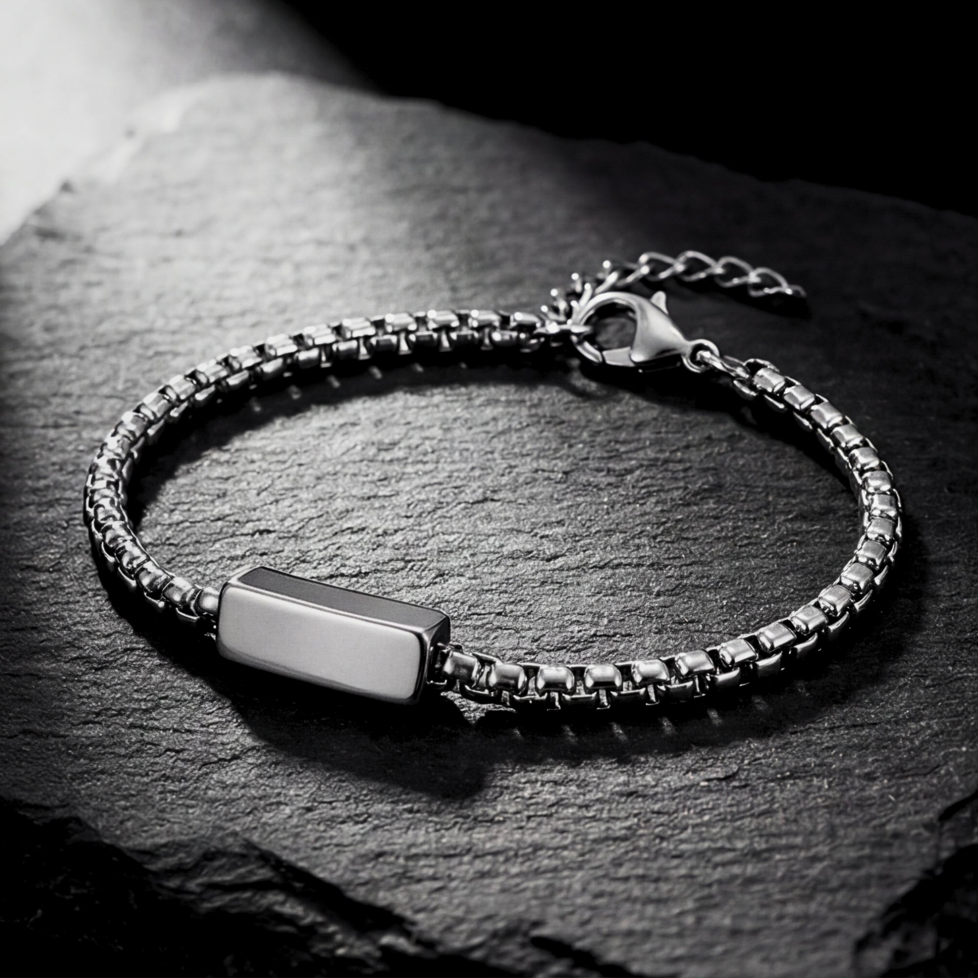 Angled view of a 5mm silver stainless steel link ID bracelet for men on a dark textured stone surface.
