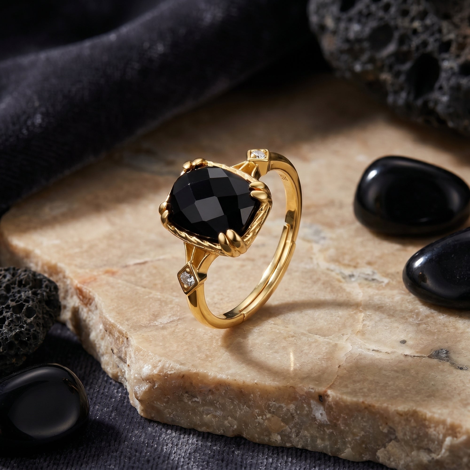 Cushion-cut natural onyx ring in 18K gold plating styled on a stone slab with black pebbles.
