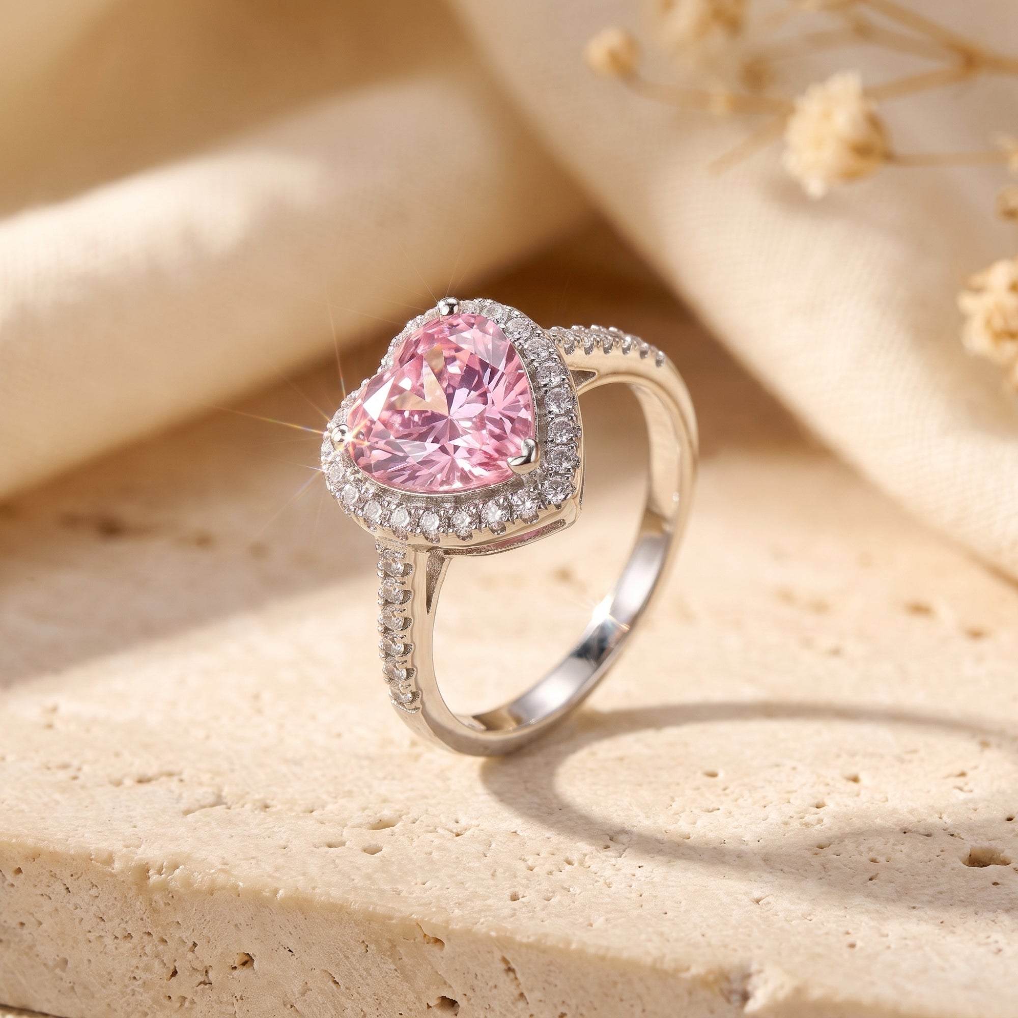 Heart-shaped simulated pink tourmaline halo ring in S925 sterling silver on a stone surface with dried flowers.