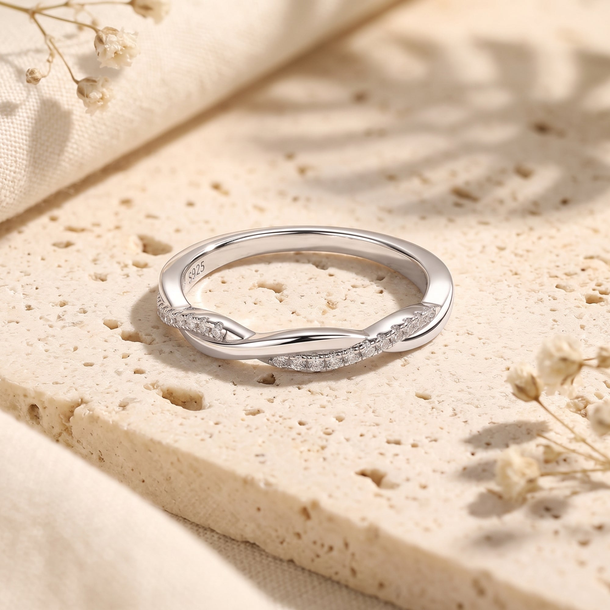 Veronelle twisted sterling silver promise ring with pavé simulated diamonds on a textured stone surface.