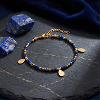 Gold plated stainless steel faceted 3mm lapis bead bracelet with teardrop charms on slate with raw stones.