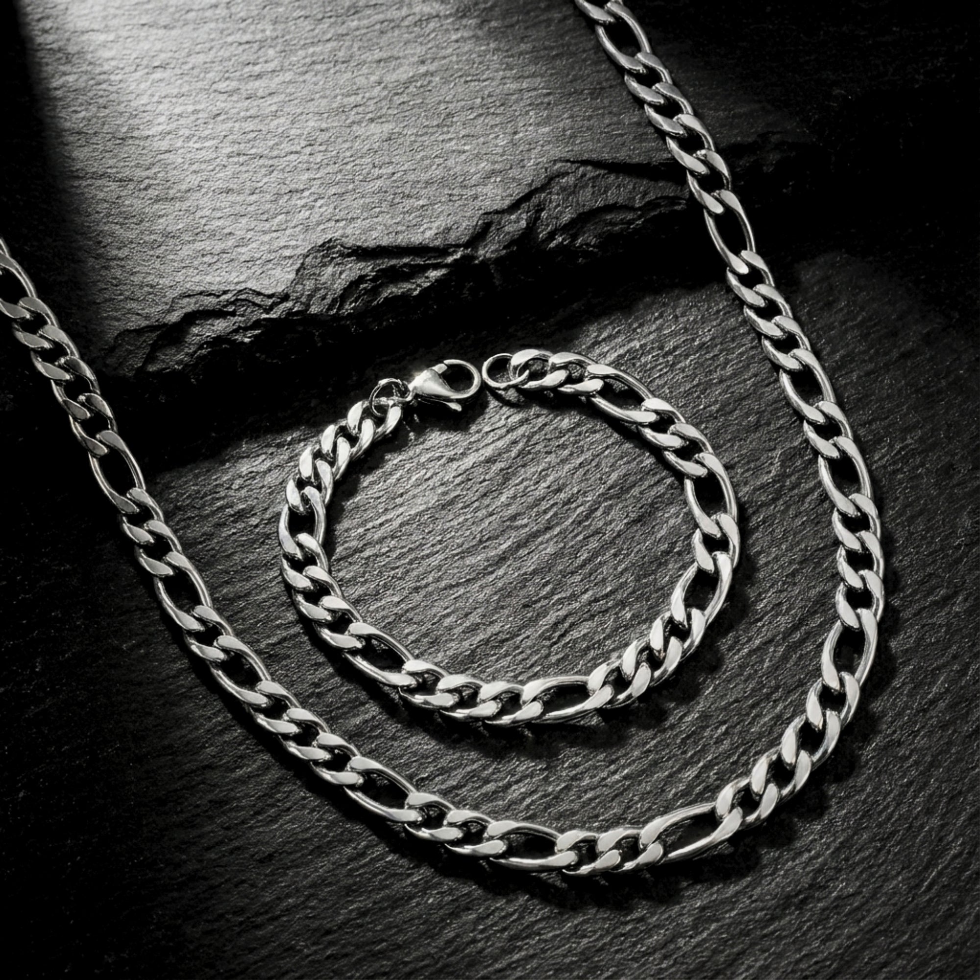 Silver 8mm stainless steel Figaro chain and bracelet set displayed on a dark textured stone surface.