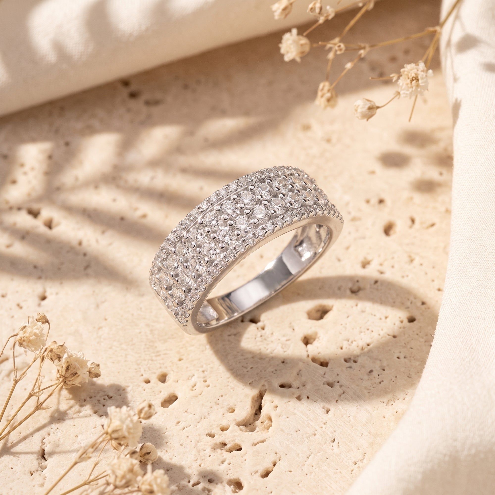 Multi-row cubic zirconia sterling silver promise ring on a textured stone surface with floral accents.