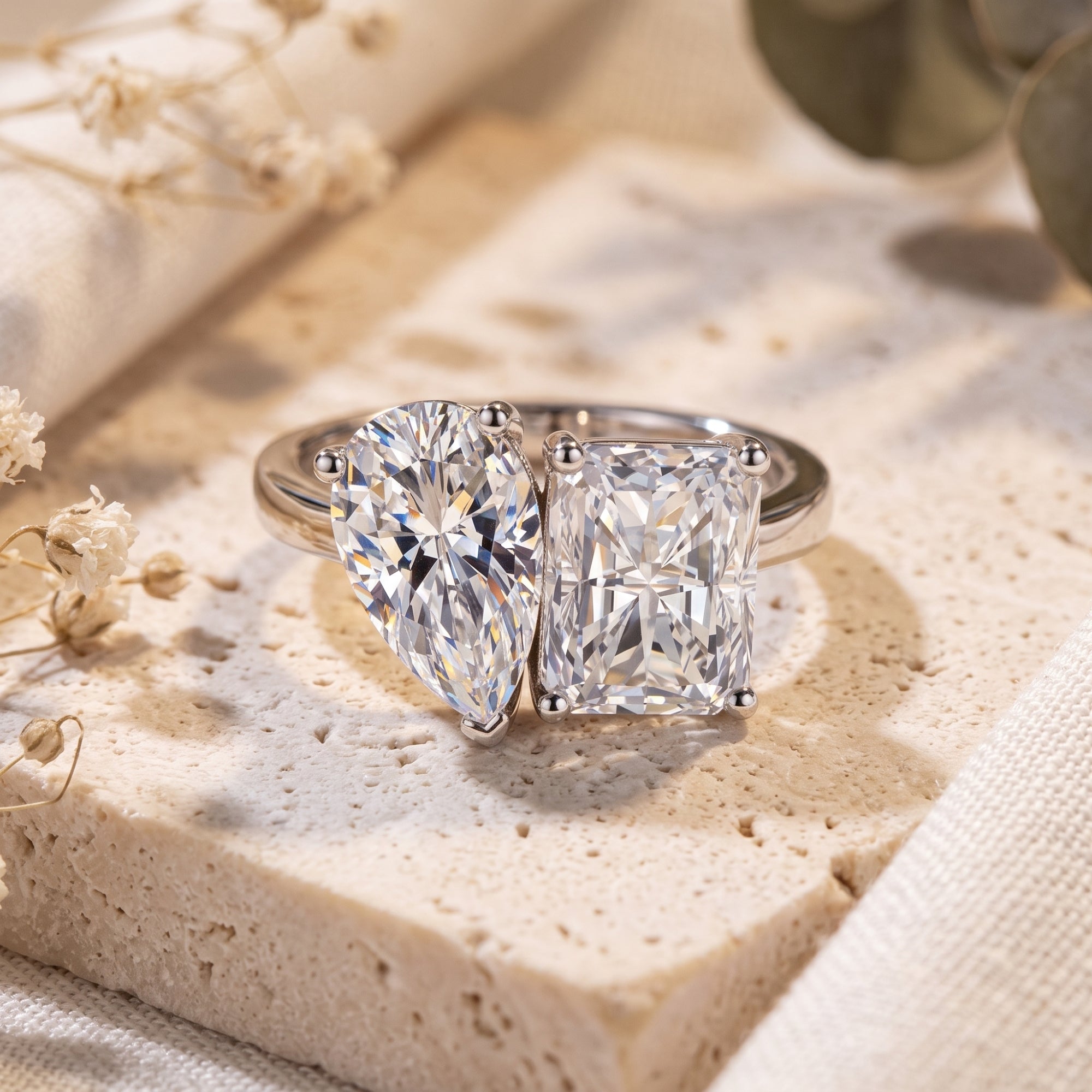 Toi et Moi silver ring with pear and radiant simulated diamonds on a stone surface.