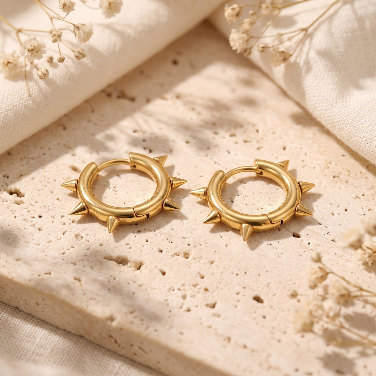 Pair of gold-color spiked hoop earrings resting on a porous beige stone surface.