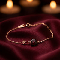 18K rose gold heart-cut garnet bracelet with a star charm displayed on burgundy silk fabric.
