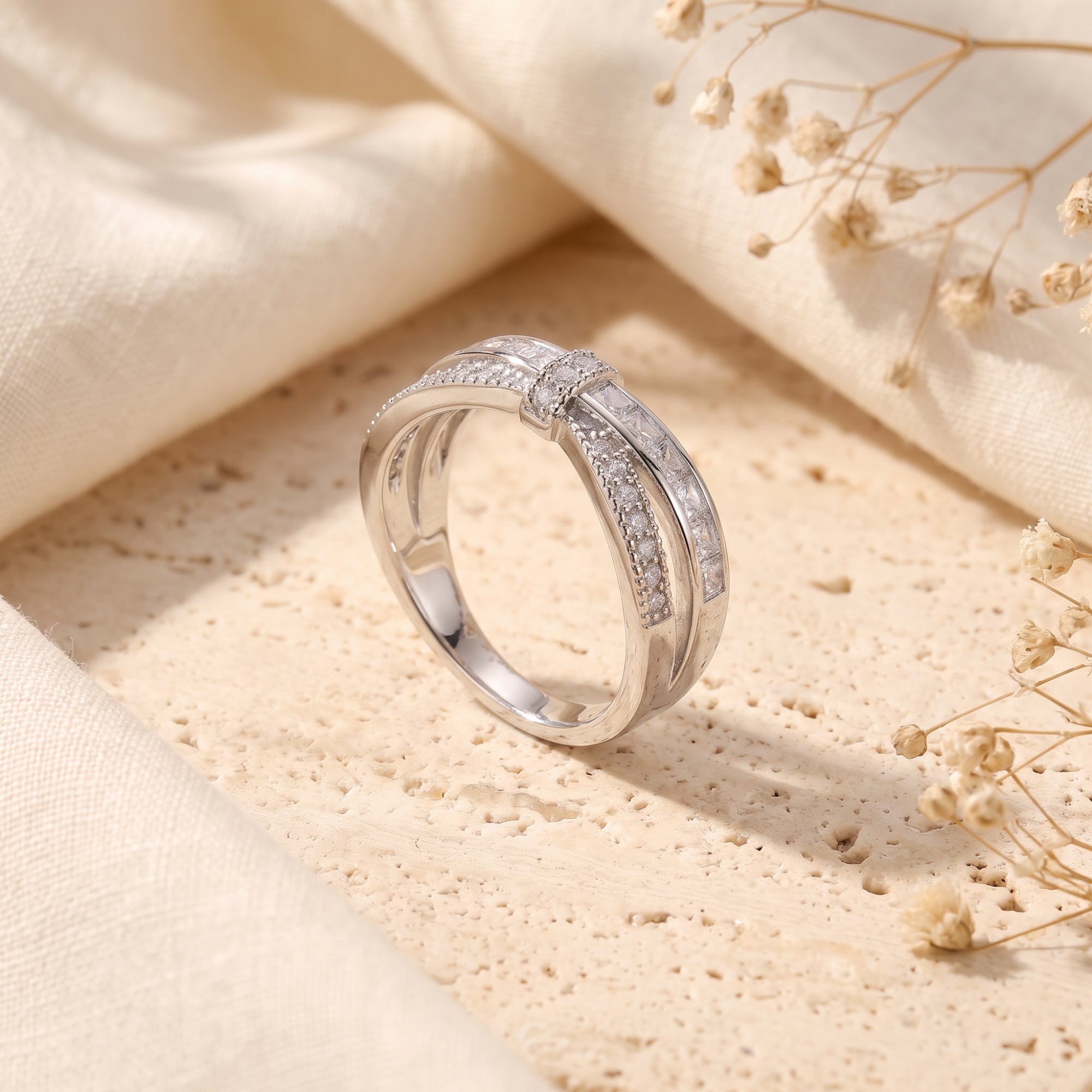 Charlotte silver ribbon promise ring with criss-cross CZ bands on a textured stone and fabric background.