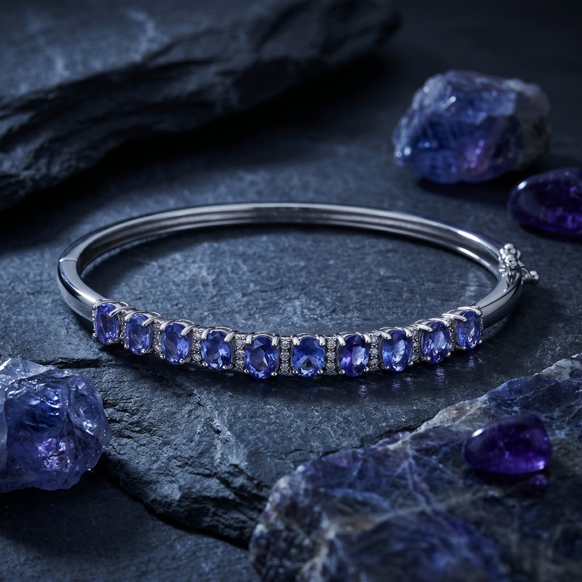 Silver oval tanzanite line bracelet styled on dark volcanic rock with raw purple gemstone crystals.