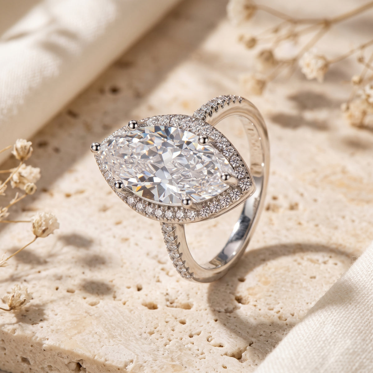 Close-up of a silver ring with a large marquise-cut clear center stone, sparkling halo, and pavé band.