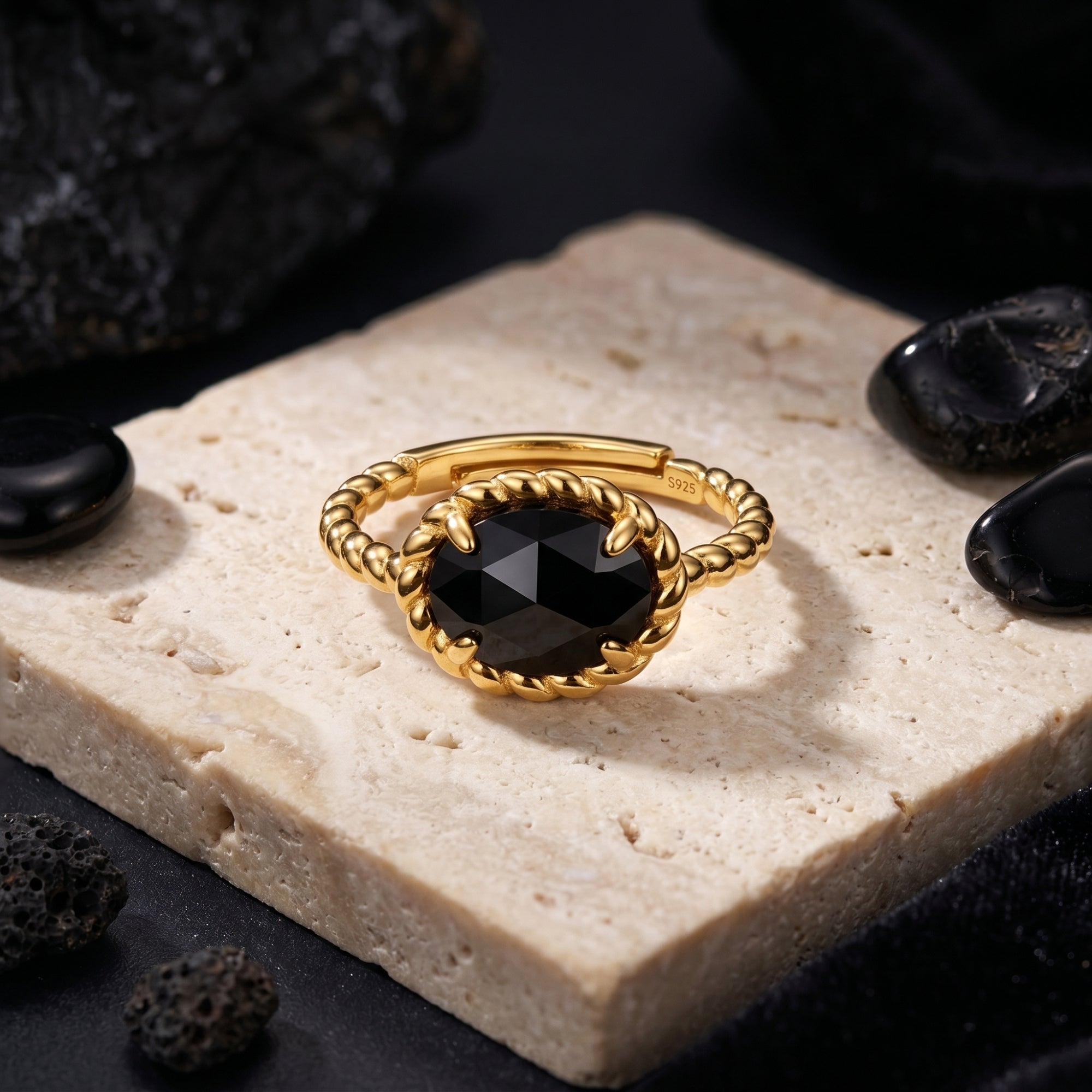 Oval-cut black onyx ring in 18K gold plated silver with a twisted band, styled on a stone slab.