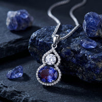 Oval tanzanite pendant necklace in 10K, 14K, or 18K solid white gold resting on raw blue gemstones.