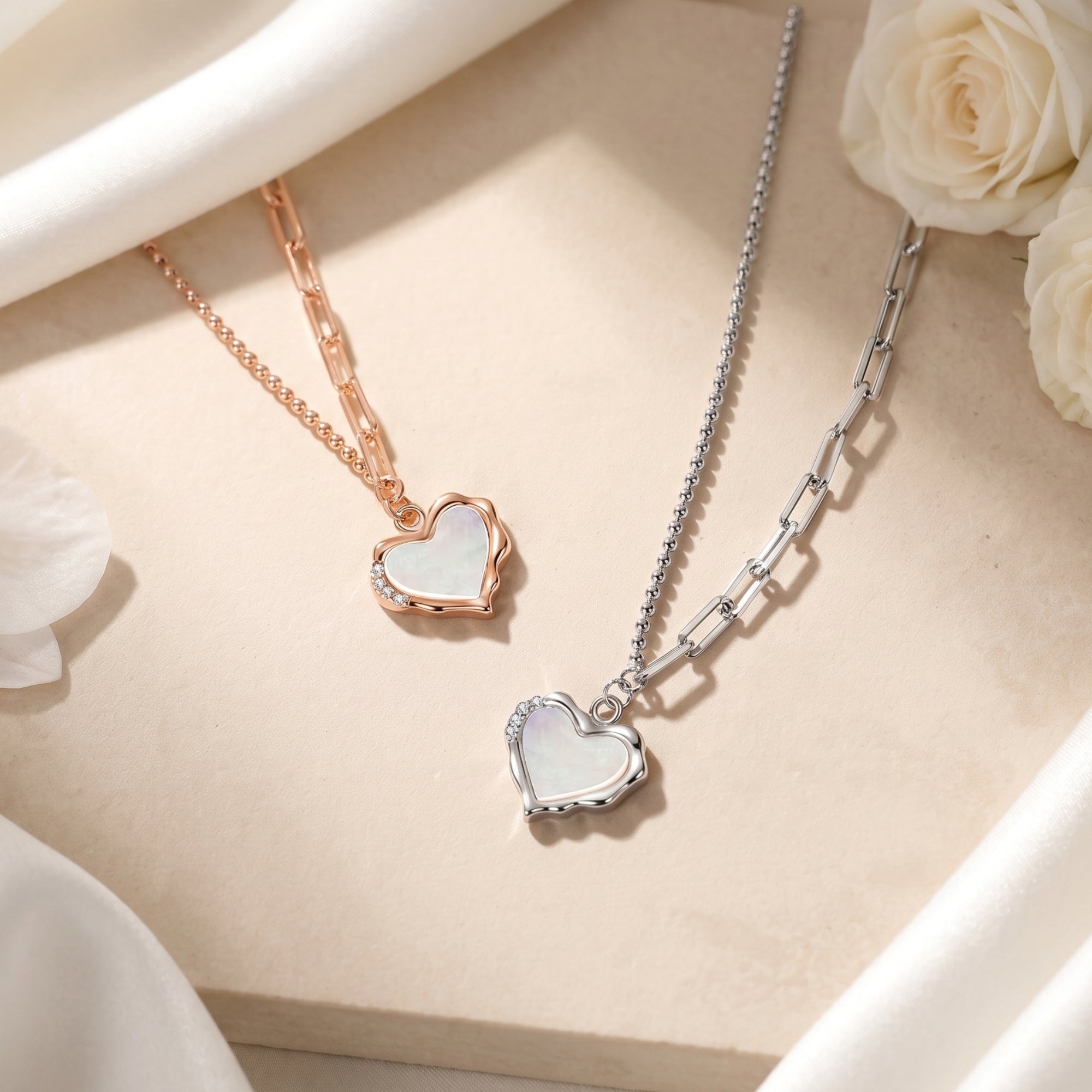 Rose gold and silver heart necklaces with white opal pendants on a stone surface with roses.