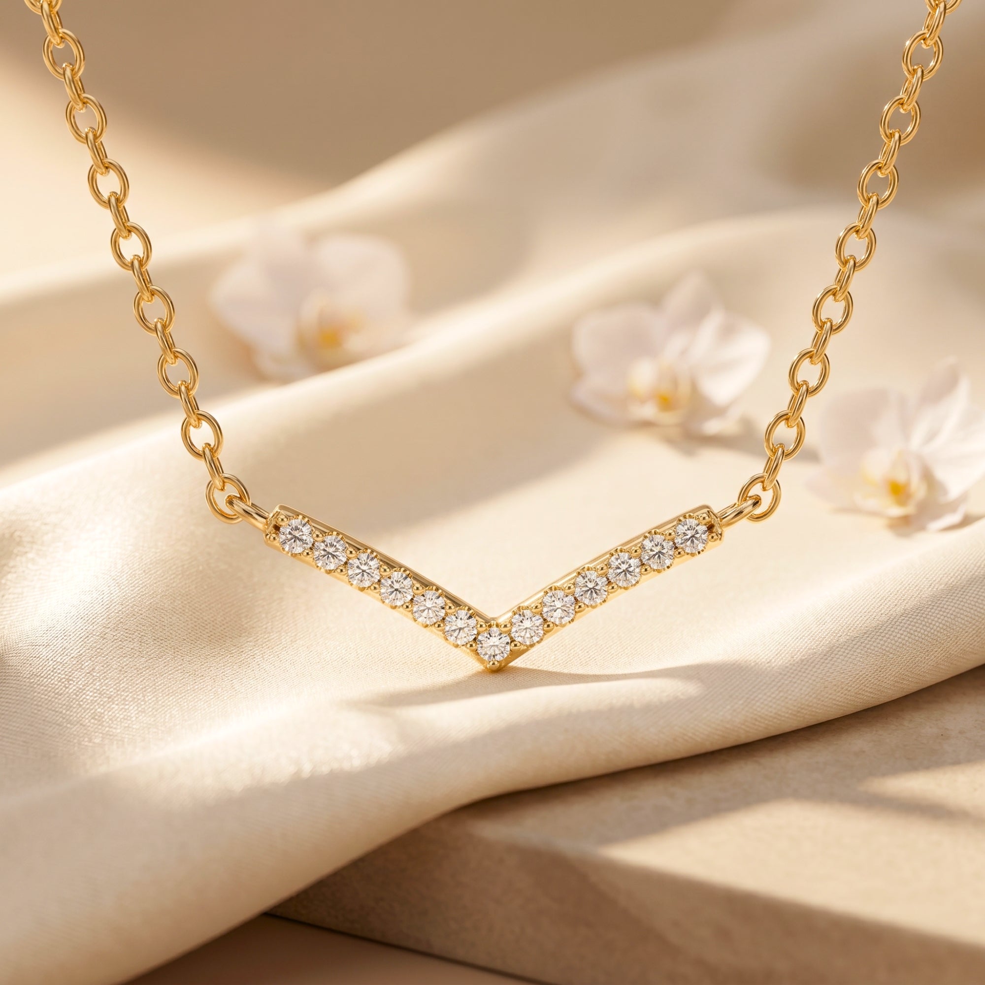 Gold chevron moissanite station necklace on draped silk with flowers.