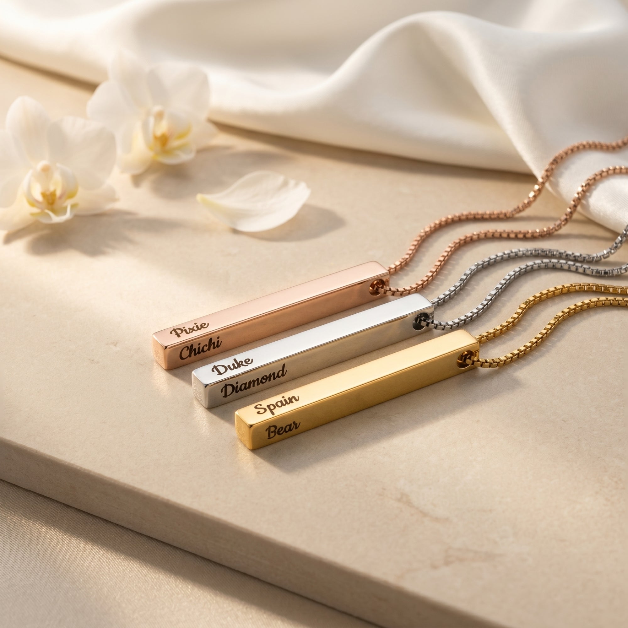 Three engraved bar necklaces in rose gold, silver, and gold on a styled lifestyle background.