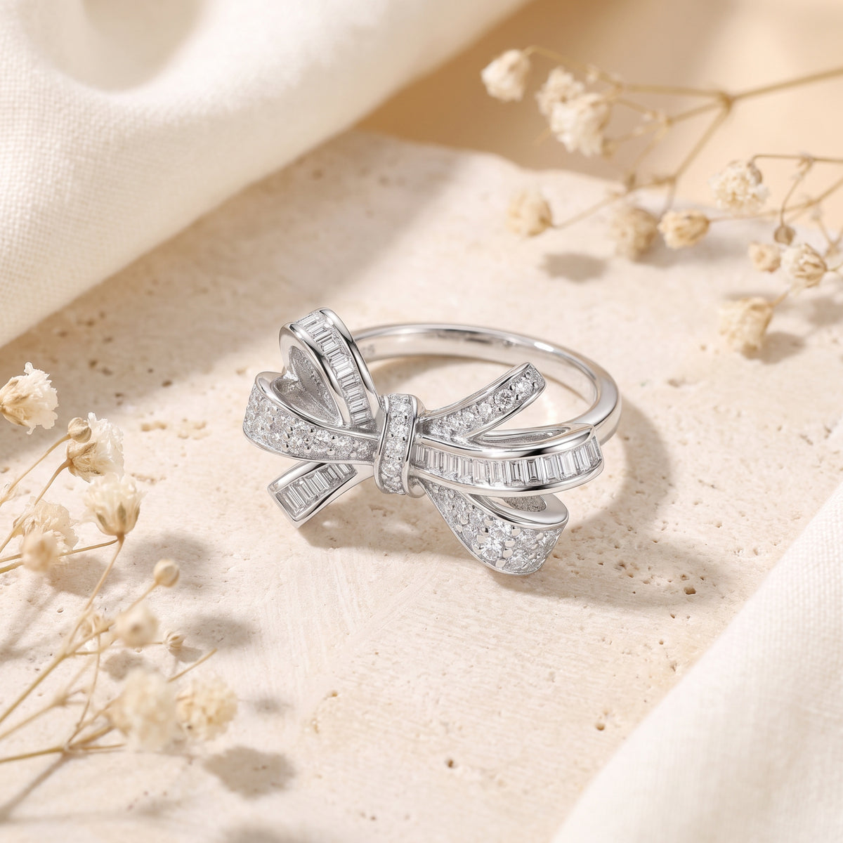 Sterling silver bow ring with baguette and pavé diamonds on a stone lifestyle background.