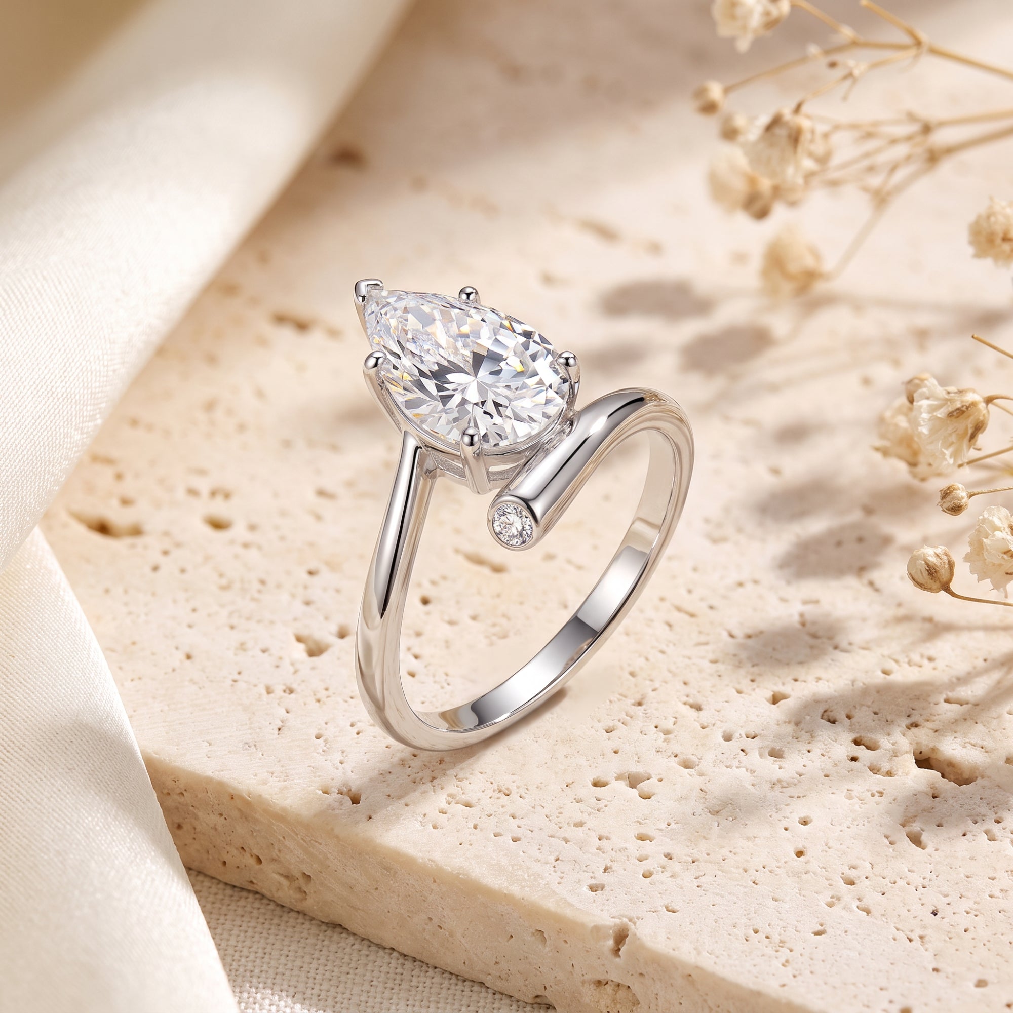 Pear-cut simulated diamond bypass ring in S925 sterling silver on a stone surface.