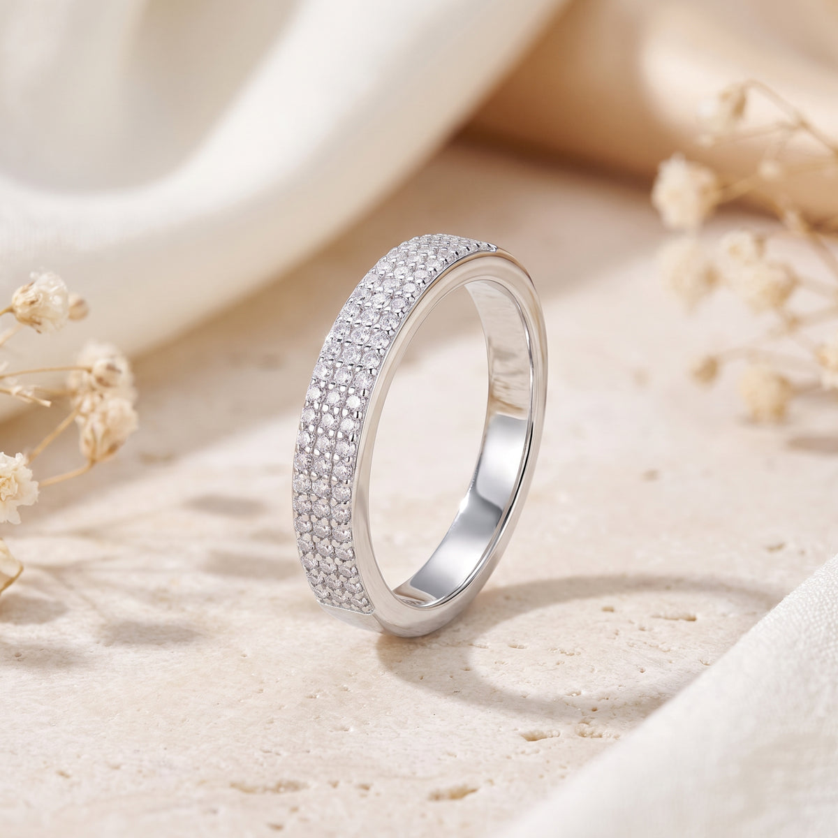 Upright silver band ring with three rows of micro-pavé clear stones on a textured beige surface.