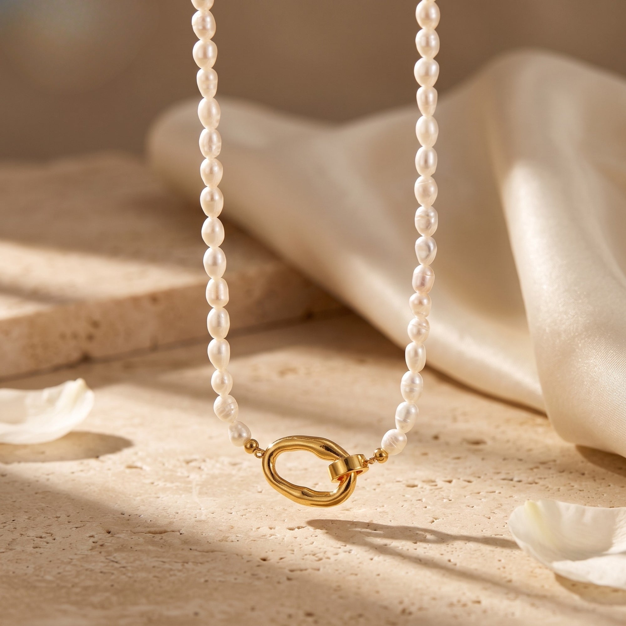 Audrielle 18K gold PVD pearl necklace with white rice pearls on textured surface.