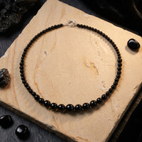 Top-down view of a graduated natural black onyx bead necklace with a clasp on a textured stone slab.